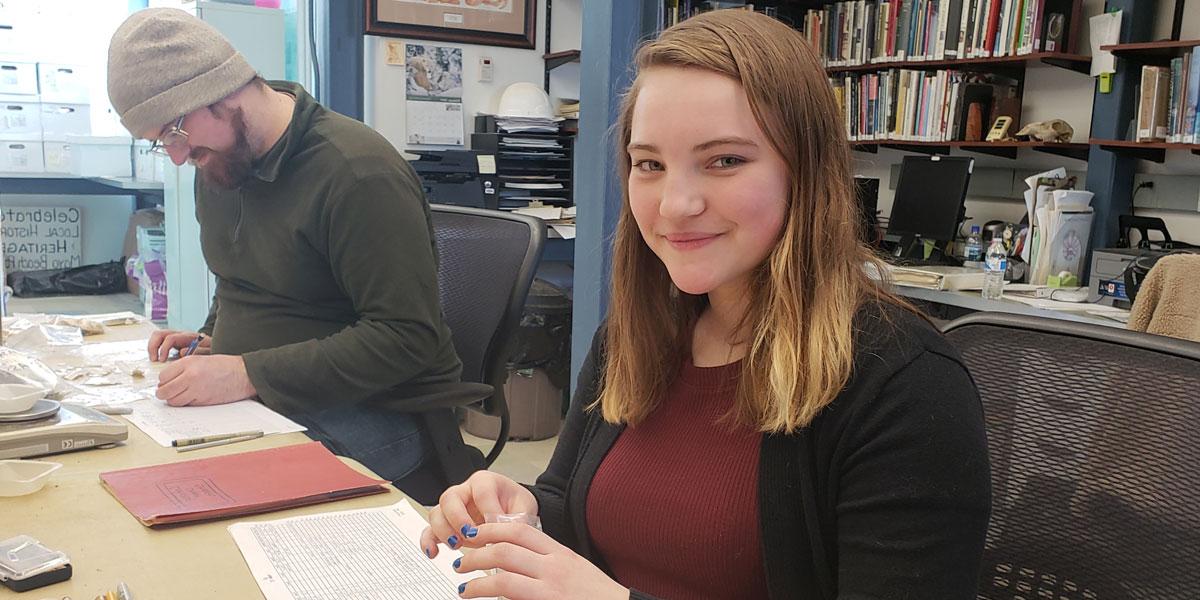 Archaeology Intern Gabrielle Rapine looking at artifacts.